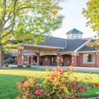 A charming brick building surrounded by well-maintained landscaping, featuring vibrant flowers and mature trees.