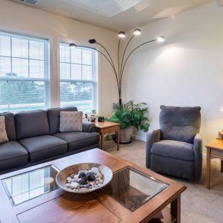 A cozy living room with a sofa, armchair, coffee table, and large windows.