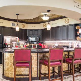 A modern kitchen with a bar area featuring red chairs and black cabinets.