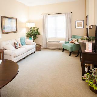 A cozy and well-lit living room with a sofa and armchair, complemented by decorative elements and a large window.