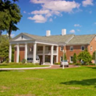 A large brick building with white columns and a sprawling green lawn under a partly cloudy sky.