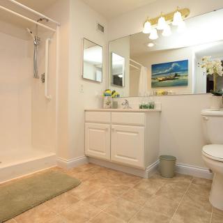 A well-lit bathroom with a shower, vanity, mirror, and toilet.