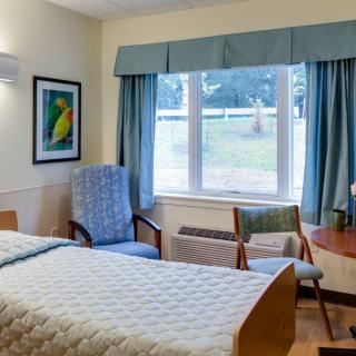 A cozy bedroom with a bed, chairs, and large window letting in natural light.