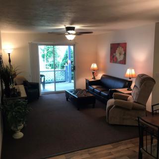 A cozy living room with a sofa, recliner, lamps, and a ceiling fan, featuring a sliding door leading to an outdoor space.