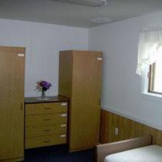 A simple bedroom featuring wooden furniture, including a wardrobe and dresser, with a vase of flowers for decoration.