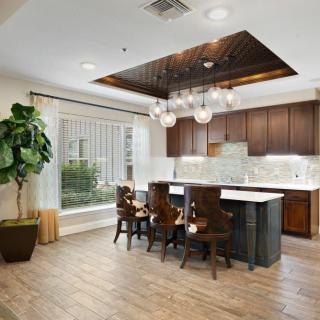 A modern kitchen interior featuring a central island with bar stools, a unique chandelier, and hardwood flooring.