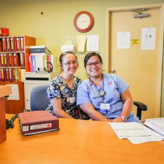Two friendly staff members smile for the camera in a healthcare office setting.