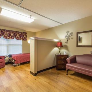 A comfortable nursing home room with a bed, sofa, and lamp.