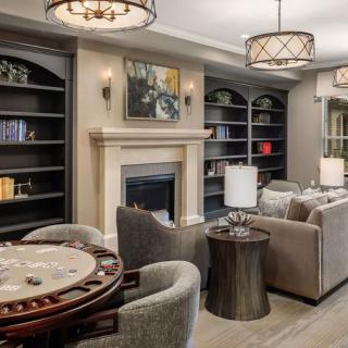 A modern living room featuring a cozy seating area, elegant chandeliers, and a decorative fireplace with bookshelves on either side.