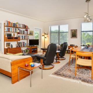 A cozy living room with a bookshelf, sofa, chairs, and dining area.