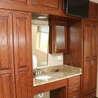 A modern bathroom vanity featuring wooden cabinets and a granite countertop, equipped with a mirror and a television.