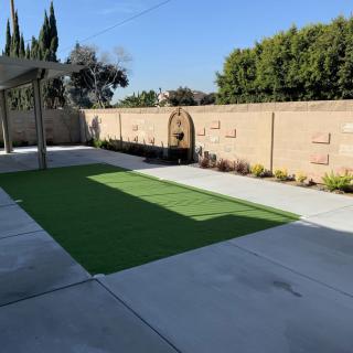 A well-maintained backyard with artificial grass and concrete patio, surrounded by a garden wall.