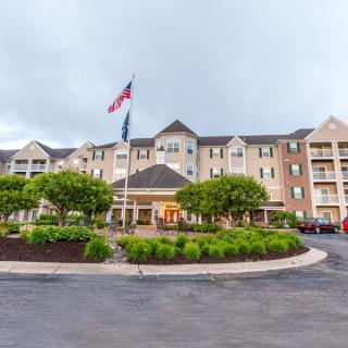 A view of a hotel exterior with a circular driveway, flags, and landscaped greenery.
