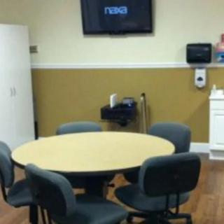 A small meeting room with a round table, several chairs, and a television on the wall.