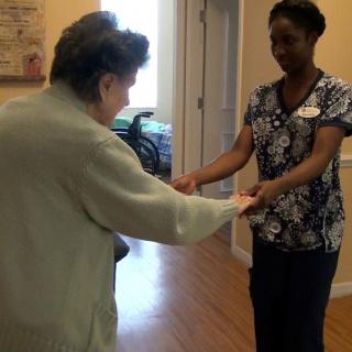A caregiver assisting an elderly person with mobility exercises in a healthcare facility.