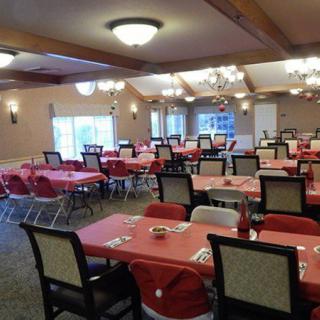 An empty dining room with tables covered in red tablecloths, arranged neatly for guests.