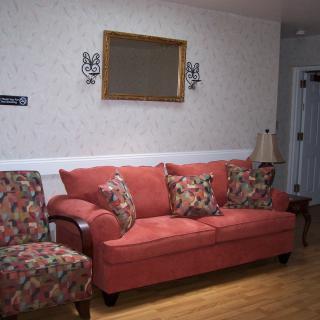 A cozy living room featuring a red sofa, an upholstered armchair, and decorative wall elements.