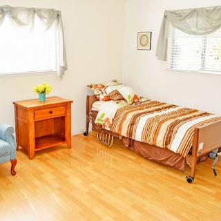 A cozy bedroom with a single bed, wooden flooring, and natural light from the windows.