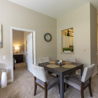 A modern dining room with a square table, cushioned chairs, and a wall clock.