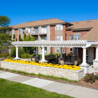 A well-maintained apartment building with a white pergola and vibrant flower landscaping on a sunny day.