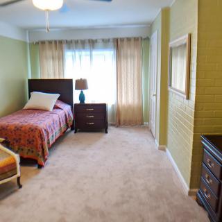 A cozy bedroom with a single bed, bedside table, and natural light from a curtained window.