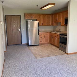 A compact apartment kitchen with wooden cabinets and stainless steel appliances.