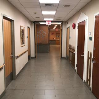 A view of a well-lit hallway in a medical facility, featuring multiple doors and tiled flooring.