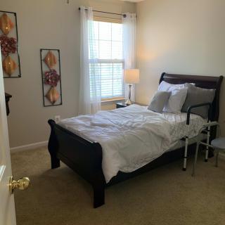 A cozy bedroom with a neatly made bed, a lamp, and decorative wall art.