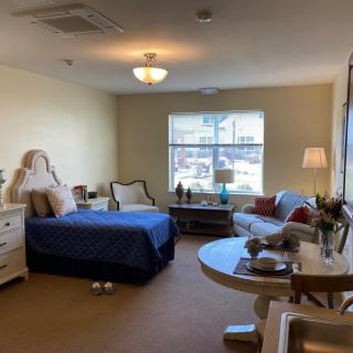 A cozy and well-furnished bedroom with a bed, a sitting area, and a large window letting in natural light.