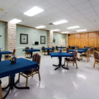 A spacious dining or meeting area featuring tables covered with blue tablecloths and several chairs, arranged in a well-lit room.