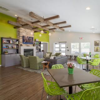 A modern interior living space with green accents, featuring a cozy seating area, wooden beam ceiling, and dining tables.