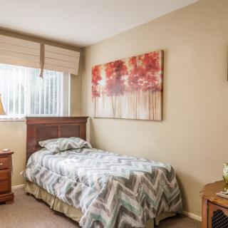 A cozy bedroom with a single bed, artwork on the wall, and a nightstand with a lamp.
