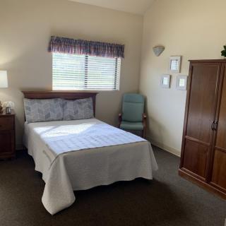 A cozy bedroom with a bed, wardrobe, and chair beside a window.
