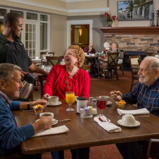 Three seniors enjoy a pleasant breakfast conversation with a waiter in a cozy dining setting.