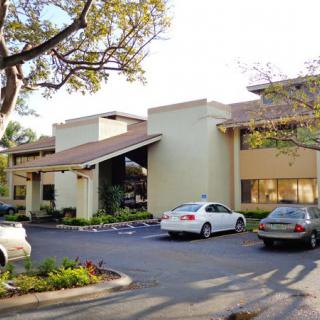 A commercial building with parked cars in a sunny parking lot.