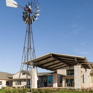 A modern building with a stone facade and an entrance canopy, featuring a windmill against a clear blue sky.