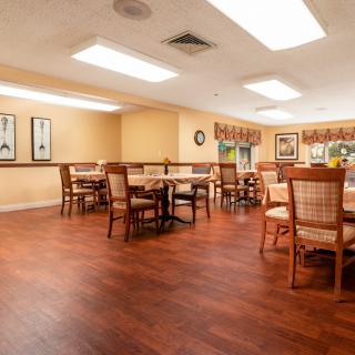 A well-lit dining room with wooden tables and chairs, featuring warm decor and artwork on the walls.
