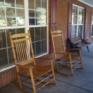 A pair of wooden rocking chairs on a porch with brick walls and large windows.