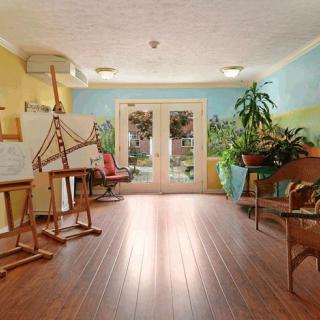 A cozy art studio with easels, paintings, and lush indoor plants under natural lighting.