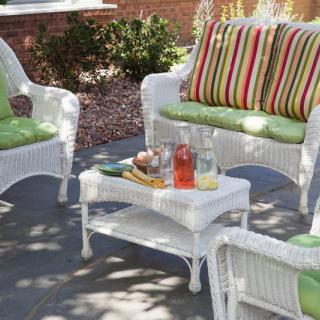 A cozy patio setup with white wicker furniture, featuring colorful striped cushions and a small table set for refreshments.