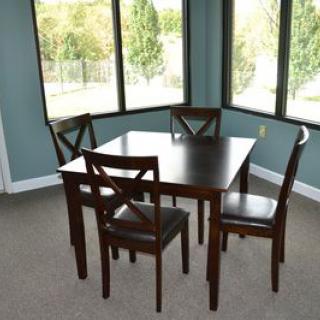 A dining area with a dark wooden table and four matching chairs near large windows that provide natural light.