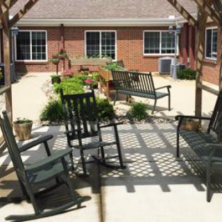 A shaded patio area featuring rocking chairs and benches surrounded by plants.