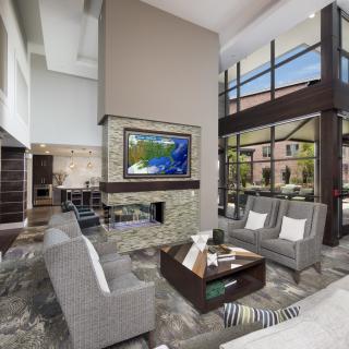 A spacious and modern living room with large windows, a central fireplace, and contemporary furnishings.