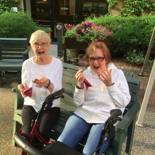 Two elderly women enjoying ice cream on a bench outdoors.