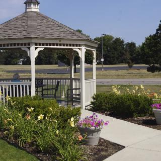 A charming white gazebo in a landscaped garden with colorful flowers and a paved walkway on a sunny day.