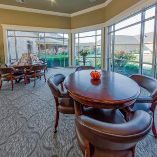 A well-lit dining area with round wooden tables and comfortable chairs, surrounded by large windows offering a view of the outside.
