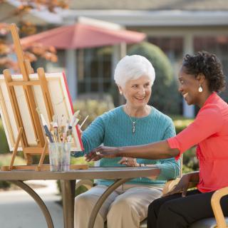 An elderly woman and an adult woman painting together outdoors.