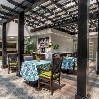 An inviting outdoor dining area with tables and chairs, covered by a decorative pergola.
