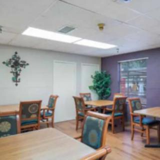 A dining room with multiple tables and chairs, featuring a wall cross decoration and indoor plant next to a window.