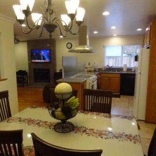 A cozy dining area with a view into the kitchen, featuring a chandelier and a television in the background.